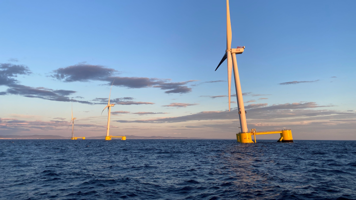 three offshore wind turbines on yellow floating platforms in the ocean, under a warm glow from the sun, showcasing renewable energy and sustainability