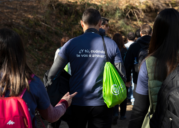 a group of individuals walking through a wooded area, led by a person wearing a dark blue shirt with the phrase in spanish 'and you, when will you dare?' they carry various backpacks, including a bright green drawstring bag