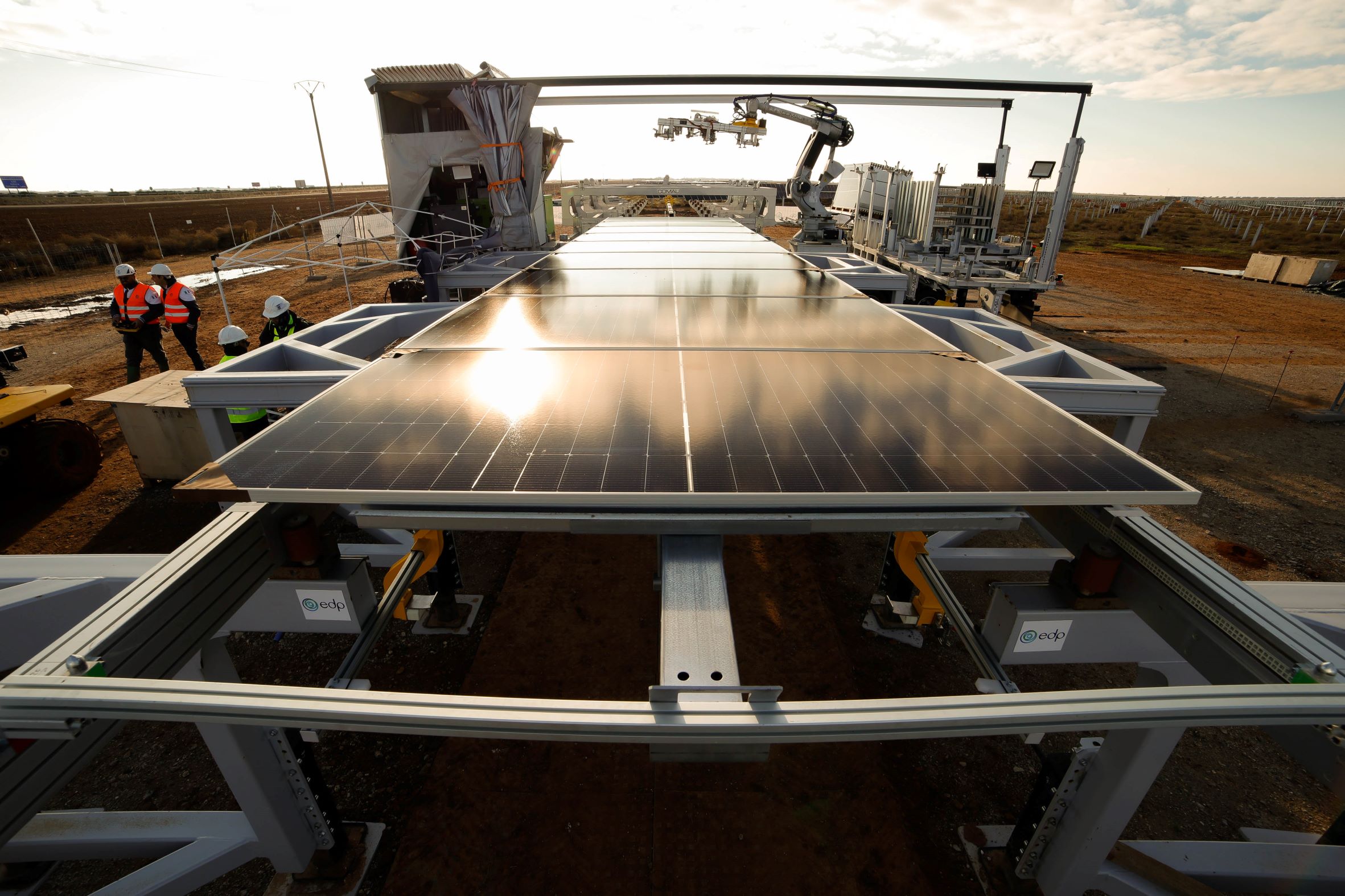 solar panel installation site using robotics, featuring mounted panels and a robotic arm assisting with positioning, while workers in safety gear oversee the process