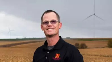 man wearing sunglasses and smiling in front of wind turbines